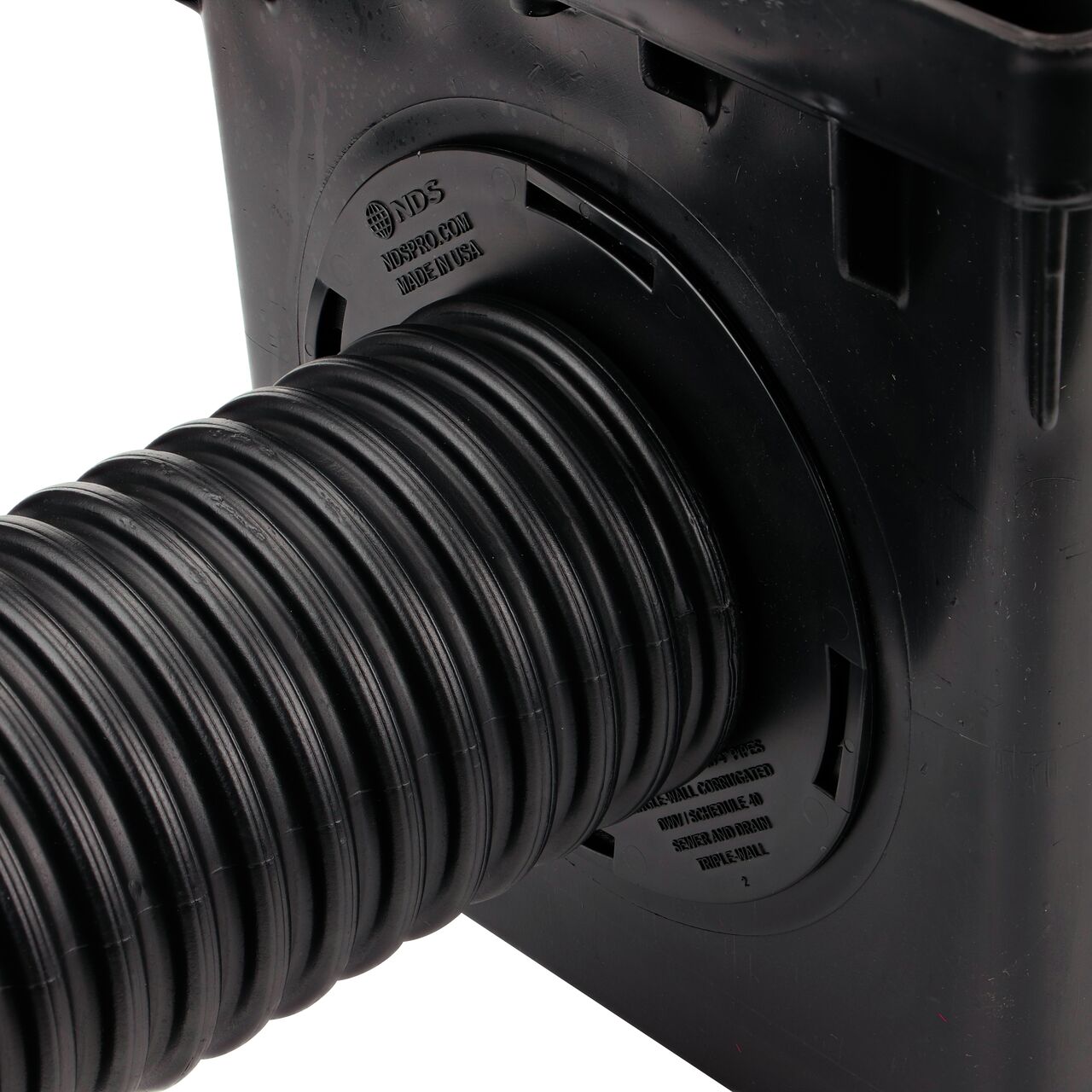Closeup of the retail (NDS 1244*) Outlet Adapter for Catch Basin Drain which fits 3 in. & 4 in. Drain Pipes, with a 4 in. single-wall corrugated pipe installed on the 3-outlet 12 in. Catch Basin Drain (NDS 1203)